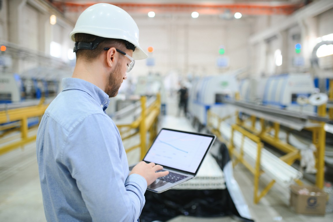 Side view of technician or engineer with headset and laptop standing in industrial factory